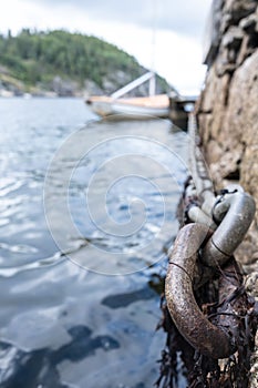 Iron chain on old stone pier, sea waves and moored sailboat and rocky shore out of focus. Bottom view.