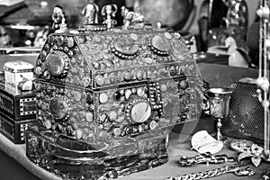 Iron chest full of stones and jewels on a table. There are golden pieces together and other objects. [Black and white version]