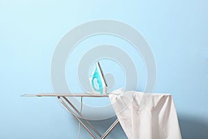 Iron and a clothes on an ironing board on a colored background.