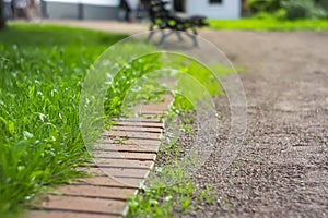 iron drainage grate on the roadside with green grass and stone pebbles at the granite curb along the pedestrian pavement of brick