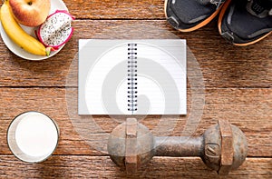 Iron dumbbell,Sports shoes and notebook with milk and fruit (banana,appke,dragon fruit) on wooden floor.