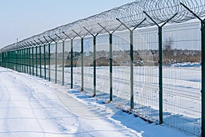 Iron fence with barbed wire in a snow-covered winter field against a blue sky. Fenced guarded territory, no access. Area