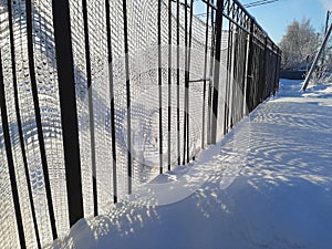 An iron fence with a stretched net slave. The sun's rays shine through the fence. Winter