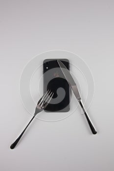 An iron fork and knife with a phone on a transparent dish.