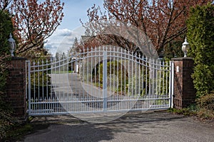 Iron front gate of a luxury home with beautiful garden. Wrought iron white gate and brick pillar