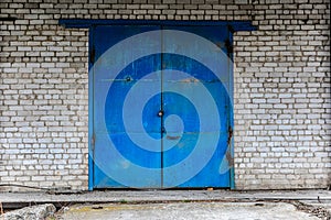 Iron gate, painted with blue paint and lock on the building of white brick.