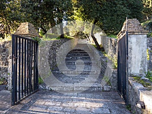 Iron gate with stone pillars to stairway with stone walls in green trees photo
