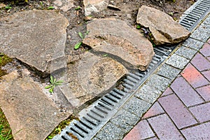 Iron grating of the drainage system near pedestrian sidewalk made of stone brick tiles.