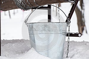 An iron gray bucket stands in the snow on wells in winter