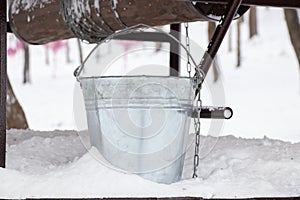 An iron gray bucket stands in the snow on wells in winter