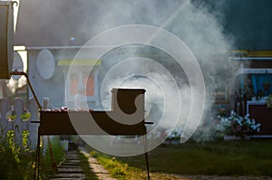 Iron grill with barbecue smokes in the rays of the setting sun on the background of a private house.