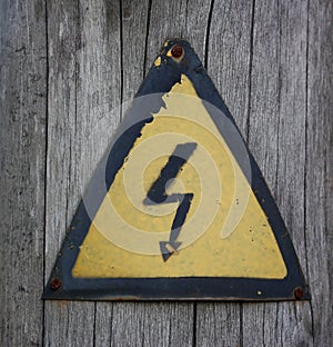 Iron high voltage sign. Nailed to a wooden post. Yellow. Closeup