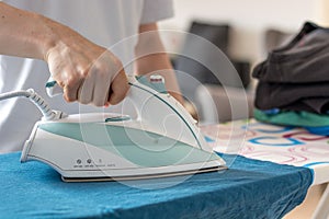 Iron on an ironing board with a blue shirt close up from the sid