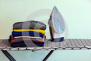 Modern iron on ironing board and a pile of clean and tidy clothes