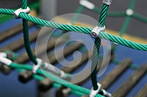 Iron joint point of ropes in children spider web with screw. Detail of cross green ropes in safety climbing outdoor equipment.