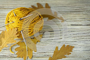 iron knitting needles and a ball of mustard-colored thread for knitting, yarn with yellow autumn oak leaves on a wooden