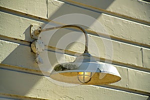 Iron metal light with protective bulb cover on side of wood panneled building brown with slats and visible exterior shadows