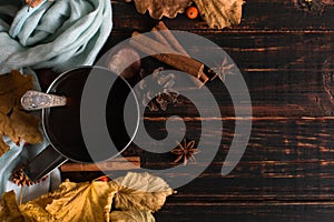 Iron mug with black coffee, spices, on a background of a scarf, dry leaves on a wooden table. Autumn mood, a warming drink. Copy