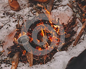 Iron mug on bonfire in snow at camping place in forest