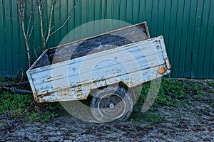 Iron old car trailer on the road near the fence