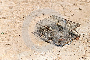 An iron old crab trap lies on a sandy beach, the traditional way of catching