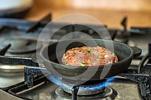 Iron pan with raw cutlet on a gas stove