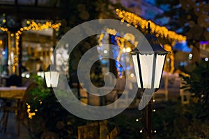 Iron retro lantern of cafe lighting glowe with warm light in the night garden.