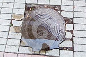 Iron round manhole cover in a puddle of water.