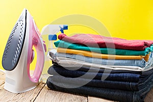 Iron and stack of colored clothes yellow background.