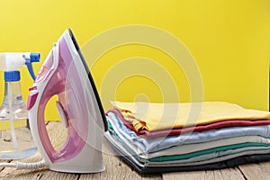 Iron and stack of colored clothes yellow background