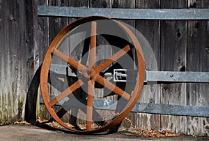 Iron Wheel Stands Rusting Against Wooden Building