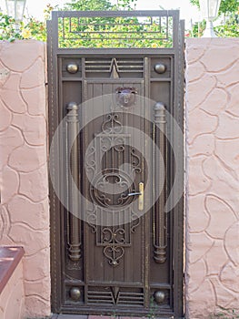 Iron wicket with wrought pattern with stone fence with pink decorative plaster