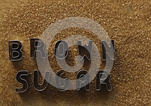 iron word - brow sugar made from metal letters on pile of dark Brown sugar.  on white table background