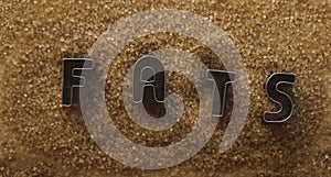 iron word - fats made from metal letters on pile of dark Brown sugar.  on white table background