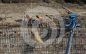 Iron workers shoveling dirt on wall of rebar and steel beams on freeway construction project