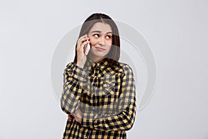 Ironic young beautiful girl dressed in plaid shirt speaking on phone, looking at side over white background.