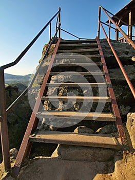 The irony wooden ladder with bended steel handrail in touristic path to viewpoint. Wooden worn out steps covered by light sand