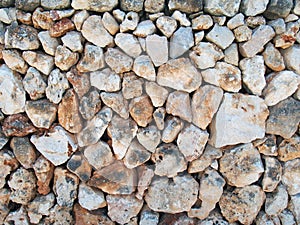 Irregular loose stone wall made of large textured brown and white limestone rocks with old twigs interwoven in the surface