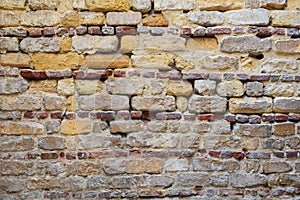 Irregular pattern of yellowish, red and gray grunge weathered uneven bricks stone wall surface