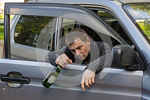 Irresponsible and drunk driver sleeps on the doors of his car with a bottle of alcoholic beverage