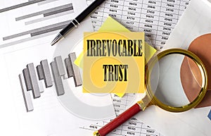 IRREVOCABLE TRUST text on a sticky on the graph background with pen and magnifier photo