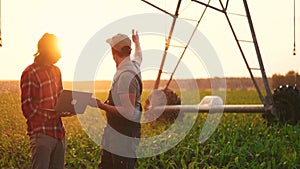 irrigation agriculture. two farmers silhouette with a laptop work in a field with corn at the back is irrigating corn