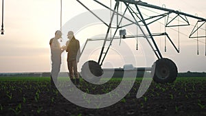 irrigation agriculture. two silhouette farmers working in the field examining installation for irrigating corn in field