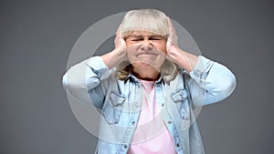 Irritated aged woman closing ears, suffering strong headache, noisy neighbors