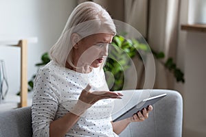 Irritated aged woman holding broken tablet having problems with gadget