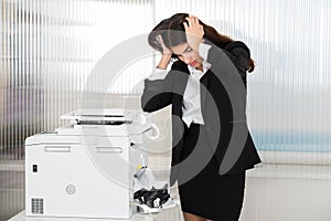 Irritated Businesswoman Looking At Paper Stuck In Printer