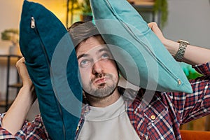 Irritated Caucasian tired bored man annoyed by noisy neighbors suffers from headache on couch
