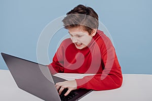 Irritated child boy in red sweatshirt typing on laptop