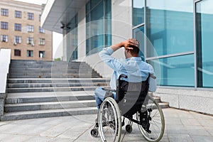 Irritated impaired black man in wheelchair having no possibility to enter building without ramp, outdoors