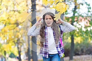 Irritated little girl suffer from loud unpleasant music sound cacophony in autumn park outdoors, headphones